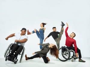 Radical Impace Dancer move dynamically across a white background. Tow dancers move in wheelchairs.