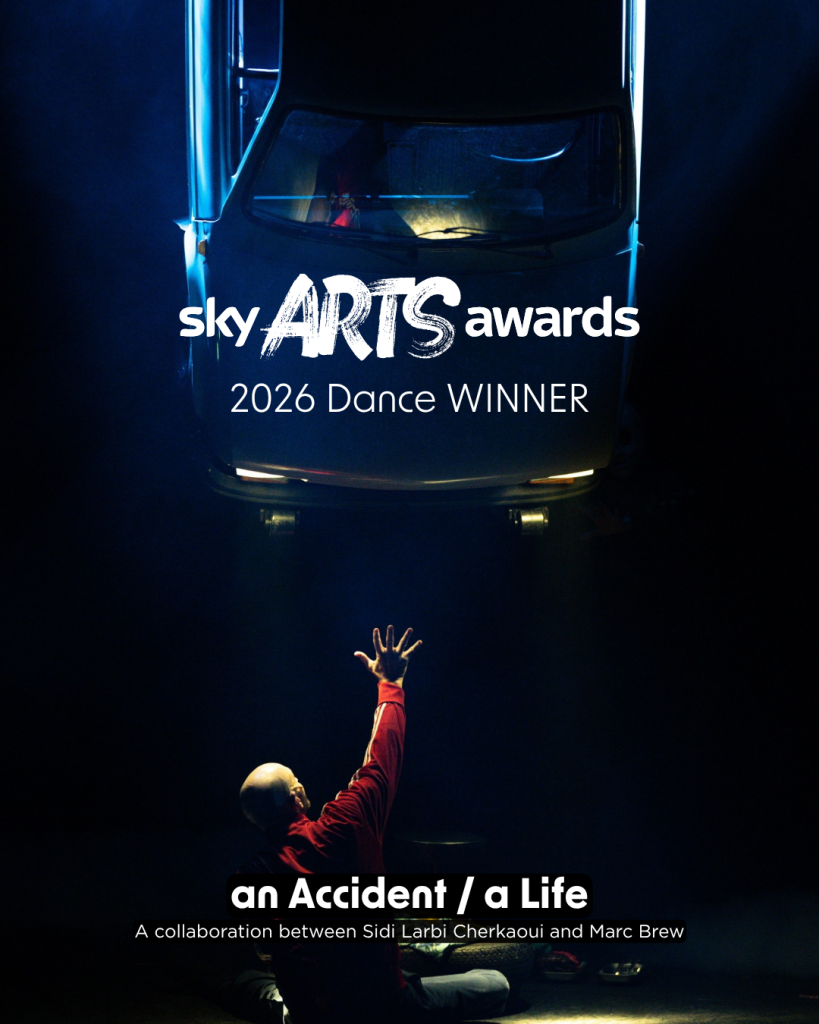 A dark stage, with a single spotlight. A car is suspended from the ceiling with its headlights shining downward onto the stage floor. Marc is underneath the car with his hand stretched upward, lit by the car headlights. The text reads “Sky Arts Awards, 2026 dance WINNER. an Accident / a Life, a collaboration between Sidi Larbi Cherkaoui and Marc Brew.